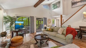A spacious living room with a large TV, a sofa, a coffee table, and a dining area.