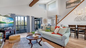 A living room with a sofa, coffee table, and TV, a dining area with chairs, and a staircase.