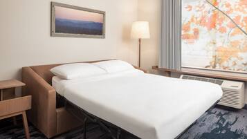 A hotel room with a bed, a desk, a lamp, a window with a view of autumn leaves, and a painting on the wall.