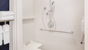 A modern shower area with a white tiled wall, a handheld showerhead, a glass-enclosed shower, and a white towel rack with folded towels.