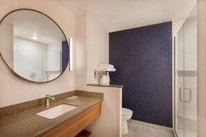 Un bany modern amb un mirall rodó, un lavabo, un vàter i una zona de dutxa.