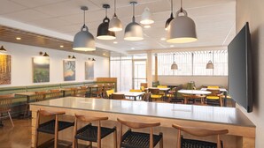 Un restaurante moderno con una larga mesa común, sillas de madera, iluminación colgante y obras de arte en las paredes.