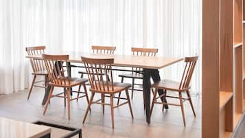 Un comedor con una mesa y sillas de madera, una estantería y un ventanal con cortinas translúcidas.