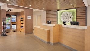 Un área de recepción con un mostrador de madera, una máquina expendedora y un elemento decorativo en la pared.
