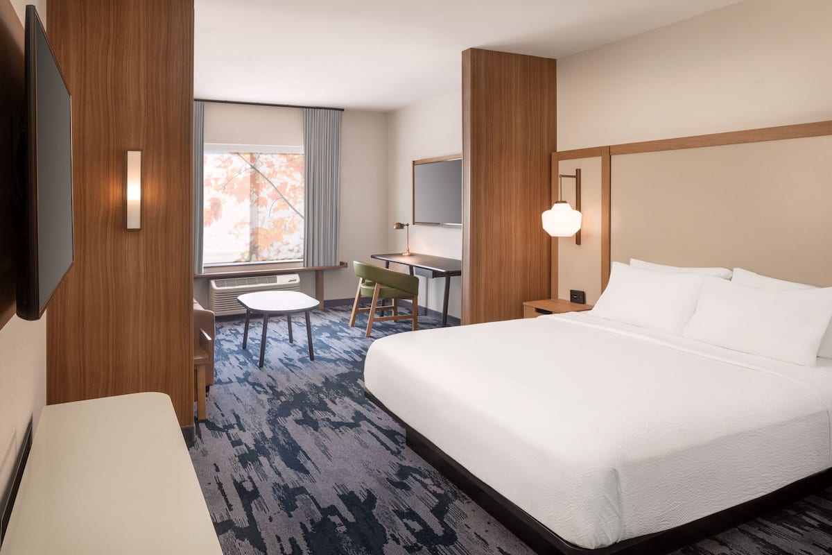 Une chambre d’hôtel avec un grand lit, un bureau, une chaise, une télévision et une fenêtre avec des rideaux.
