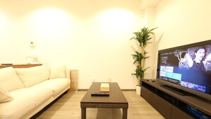 A living room with a sofa, a coffee table, a TV on a stand, and a potted plant. - Shizuka - Kozu (Osaka)
