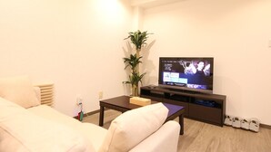 A modern living room with a flat-screen TV, a sofa, a coffee table, and a plant. - Shizuka - Kozu (Osaka)