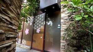 A traditional Japanese-style entrance with wooden doors and decorative patterns, stone walls, and a small garden area with plants. - Hotel mju - Adults Only (Tokyo)