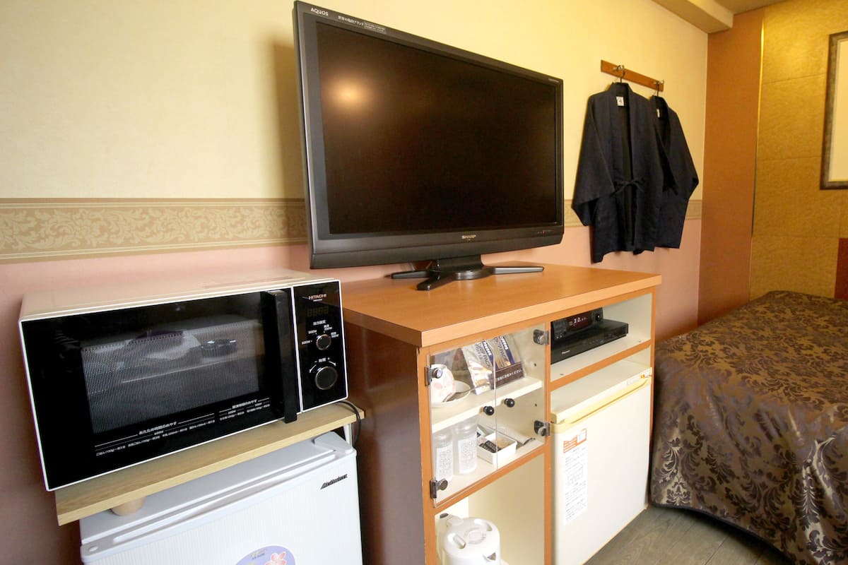 A compact hotel room with a television, microwave, and a small cabinet with various items.