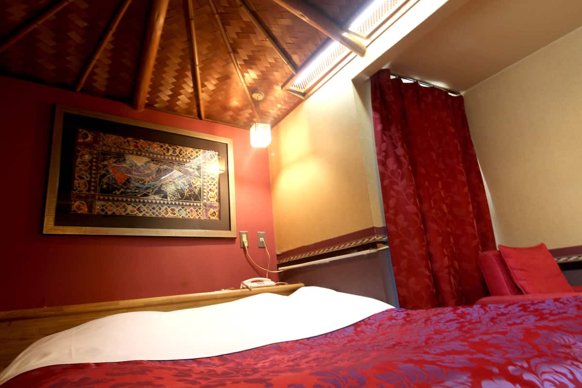 A hotel room with a bed, a wall-mounted artwork, a red curtain, and a wooden ceiling.