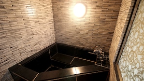 A modern bathroom with a black bathtub, tiled walls, and a decorative light fixture. - Hotel mju - Adults Only (Tokyo)