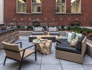 An outdoor patio with a fire pit, seating, and a brick building in the background. - WorldMark Portland - Waterfront Park (Portland)