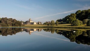 Un lago tranquilo que refleja un edificio imponente con una cúpula, rodeado de exuberante vegetación y árboles.
