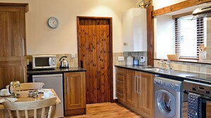 Una cocina compacta con armarios de madera, microondas, hervidor, lavadora y comedor con mesa y sillas.