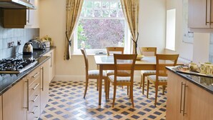 A kitchen with a gas stove, wooden cabinets, a dining table with chairs, and a window with curtains. - 1 bedroom accommodation in Windermere (Windermere)