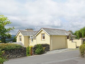 A two-story house with a stone wall and a paved driveway.