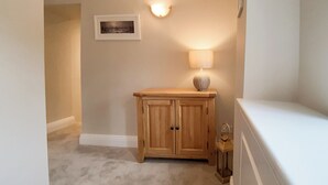 A hallway with a wooden cabinet, a wall-mounted light, and a framed picture. - 1 bedroom accommodation in Windermere (Windermere)