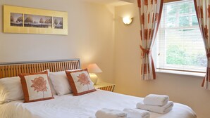 A neatly made bed with pillows, a lamp, and a window with curtains. - 1 bedroom accommodation in Windermere (Windermere)