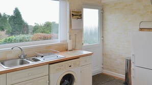 Ett litet kök med tvättmaskin, diskho och ett litet fönster.