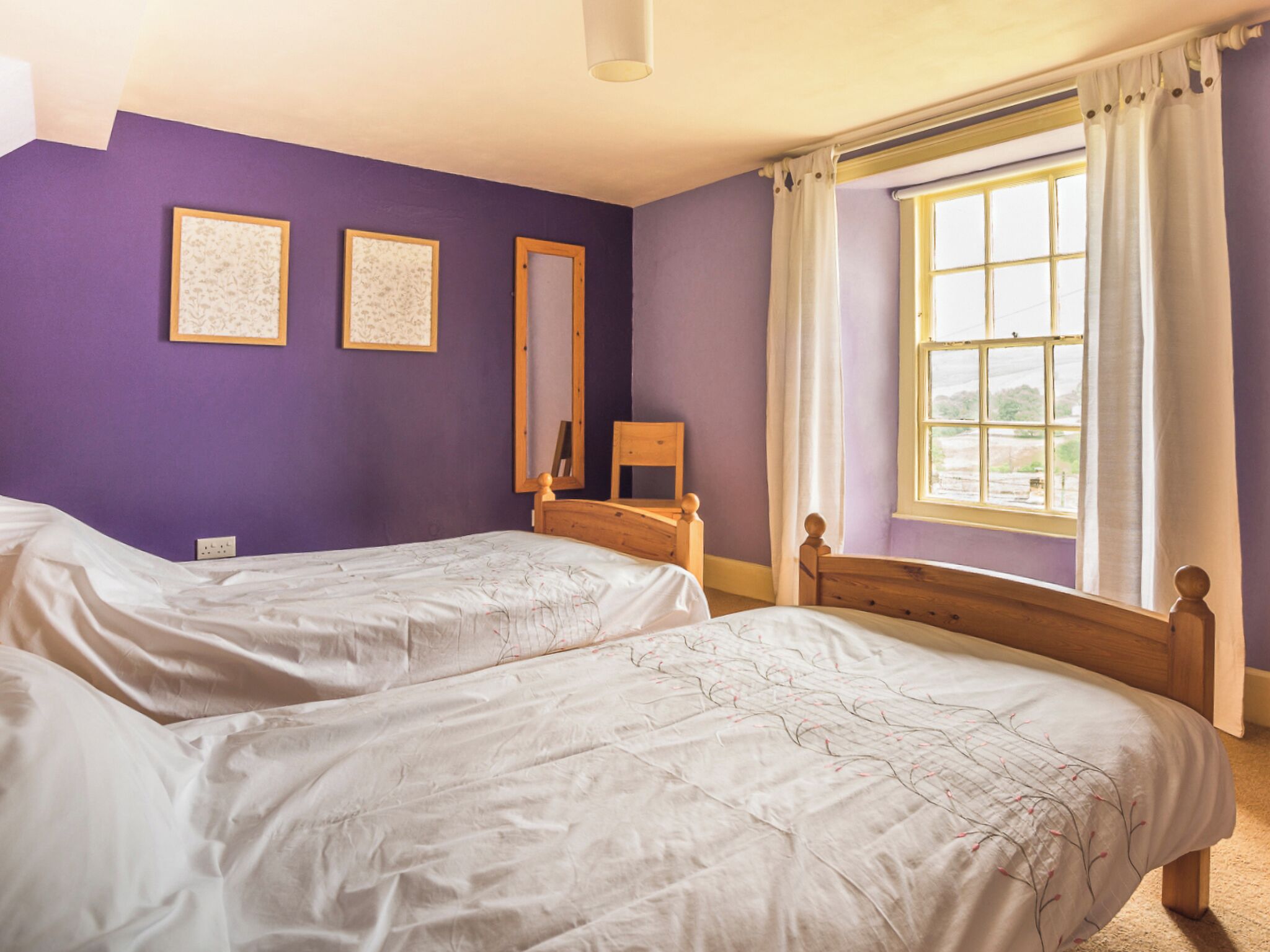 Un dormitorio con dos camas, una ventana con cortinas y dos cuadros en la pared.