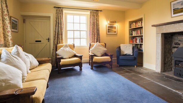 A cozy living room with a sofa, two armchairs, a fireplace, a bookshelf, and a window with curtains. - 3 bedroom accommodation in Horsehouse near Leyburn (Horsehouse near Leyburn)