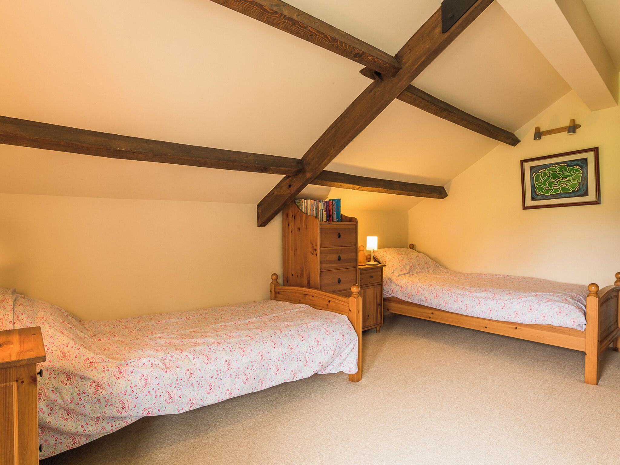 A bedroom with two single beds, a wooden dresser, and a nightstand with a lamp.
