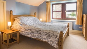 A bedroom with a wooden bed, a nightstand, a window with curtains, and a radiator. - 3 bedroom accommodation in Horsehouse near Leyburn (Horsehouse near Leyburn)