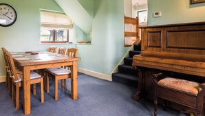 A dining area with a wooden table and chairs, a piano, and a staircase leading to another room. - 3 bedroom accommodation in Horsehouse near Leyburn (Horsehouse near Leyburn)