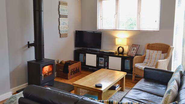 Una sala de estar acogedora con chimenea, televisor, sillón de mimbre, sofá y mesa de centro de madera.