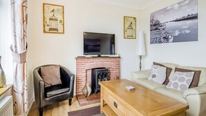 Een woonkamer met een open haard, een televisie, een bank en twee fauteuils.