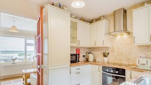 Een moderne keuken met witte kastjes, een ingebouwde oven en een raam met uitzicht op een groen landschap.
