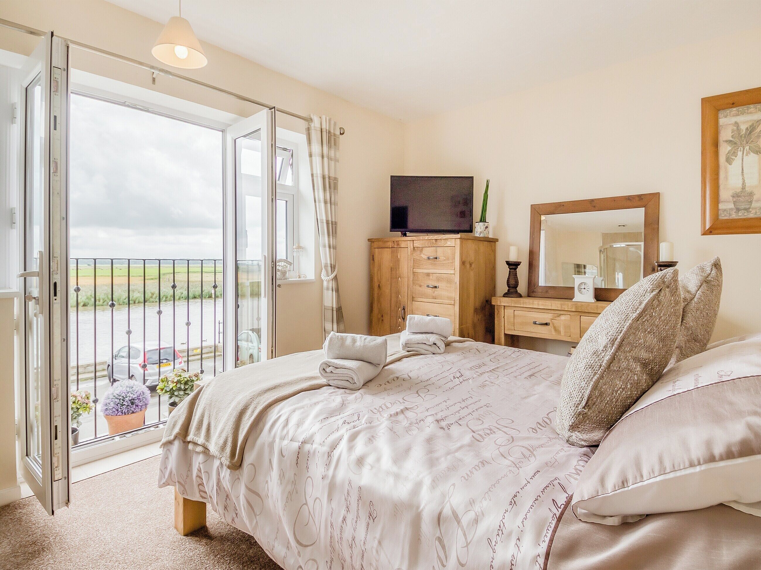 A bedroom with a bed, a dresser, a mirror, and a balcony with a view of the countryside.