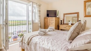 Een slaapkamer met een bed, een dressoir, een spiegel en een balkon met uitzicht op het platteland.