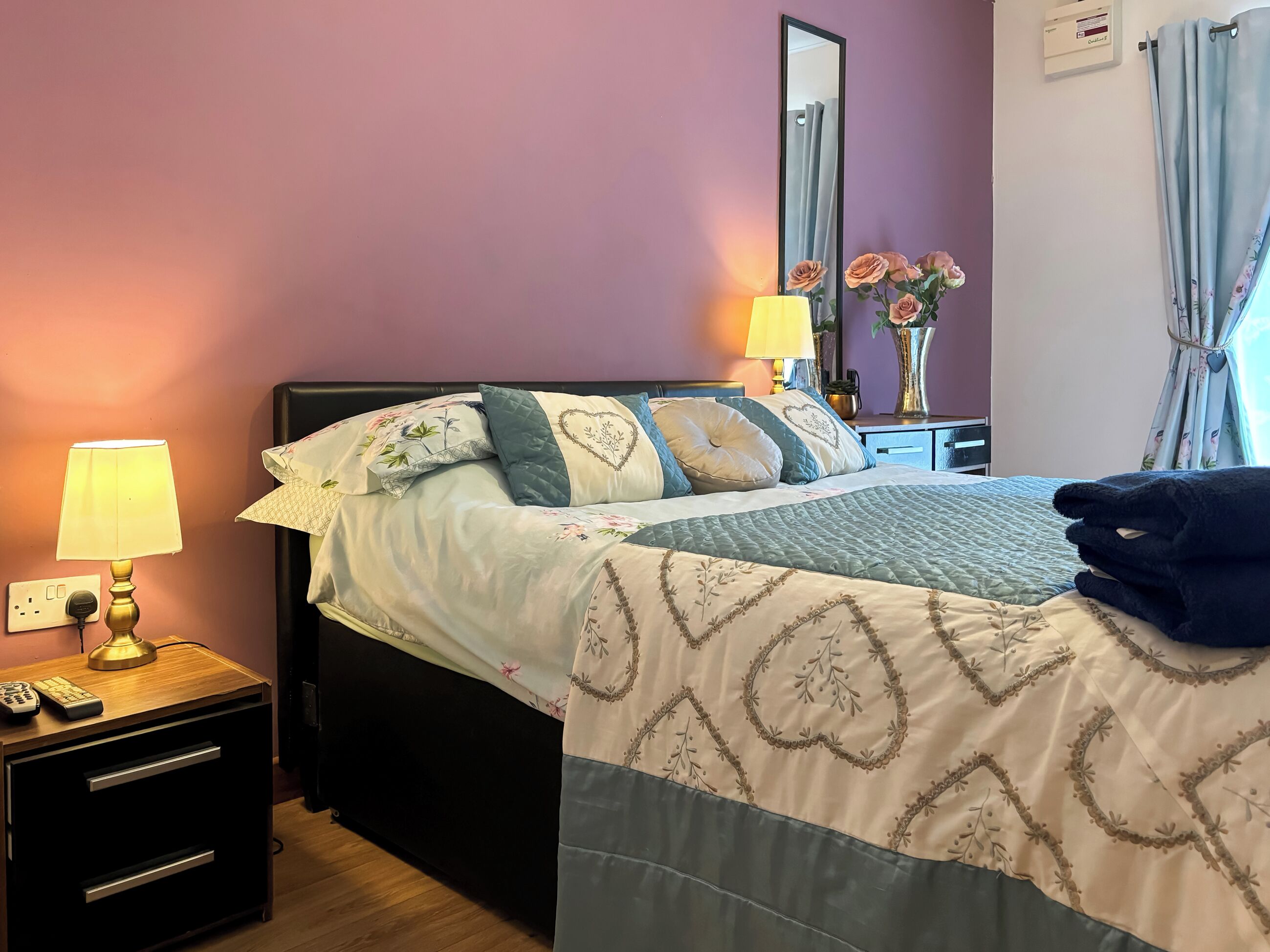A neatly made bed with floral bedding, a bedside lamp, and a nightstand with a remote control.