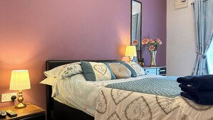 Ein ordentlich bezogenes Bett mit Blumenmuster, eine Nachttischlampe und ein Nachttisch mit Fernbedienung.