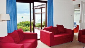 A room with two red sofas, a blue rug, and a view of the sea through a glass door.