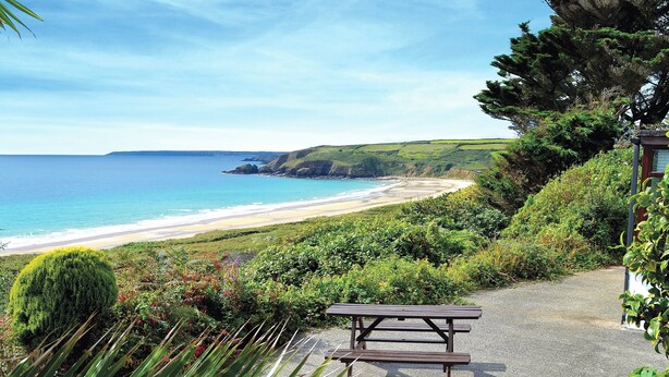 A picnic table on a gravel path with a view of a beach and ocean.