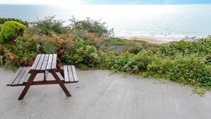 A picnic table on a concrete surface with a view of the ocean and beach in the background.