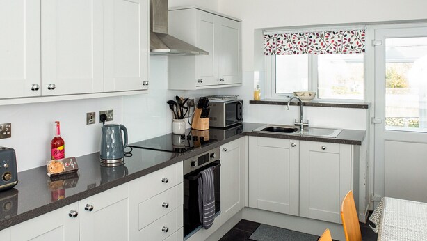 A modern kitchen with white cabinets, a stainless steel range hood, a microwave, and a sink. - 3 bedroom accommodation in Pontrug, near Caernarfon (Pontrug, near Caernarfon)