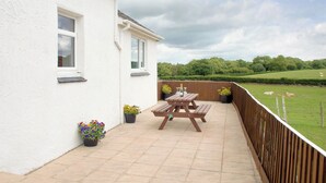 A patio with a wooden table and benches, potted plants, and a view of a green field with sheep. - 3 bedroom accommodation in Pontrug, near Caernarfon (Pontrug, near Caernarfon)