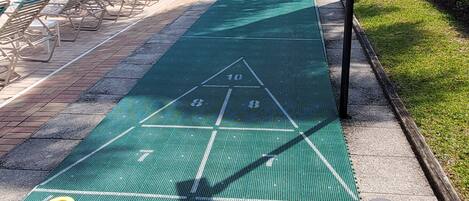 En shuffleboardbane med billardbord og liggestole i baggrunden.