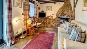Una sala de estar acogedora con chimenea de piedra, vigas de madera, un televisor y una ventana con cortinas a cuadros.