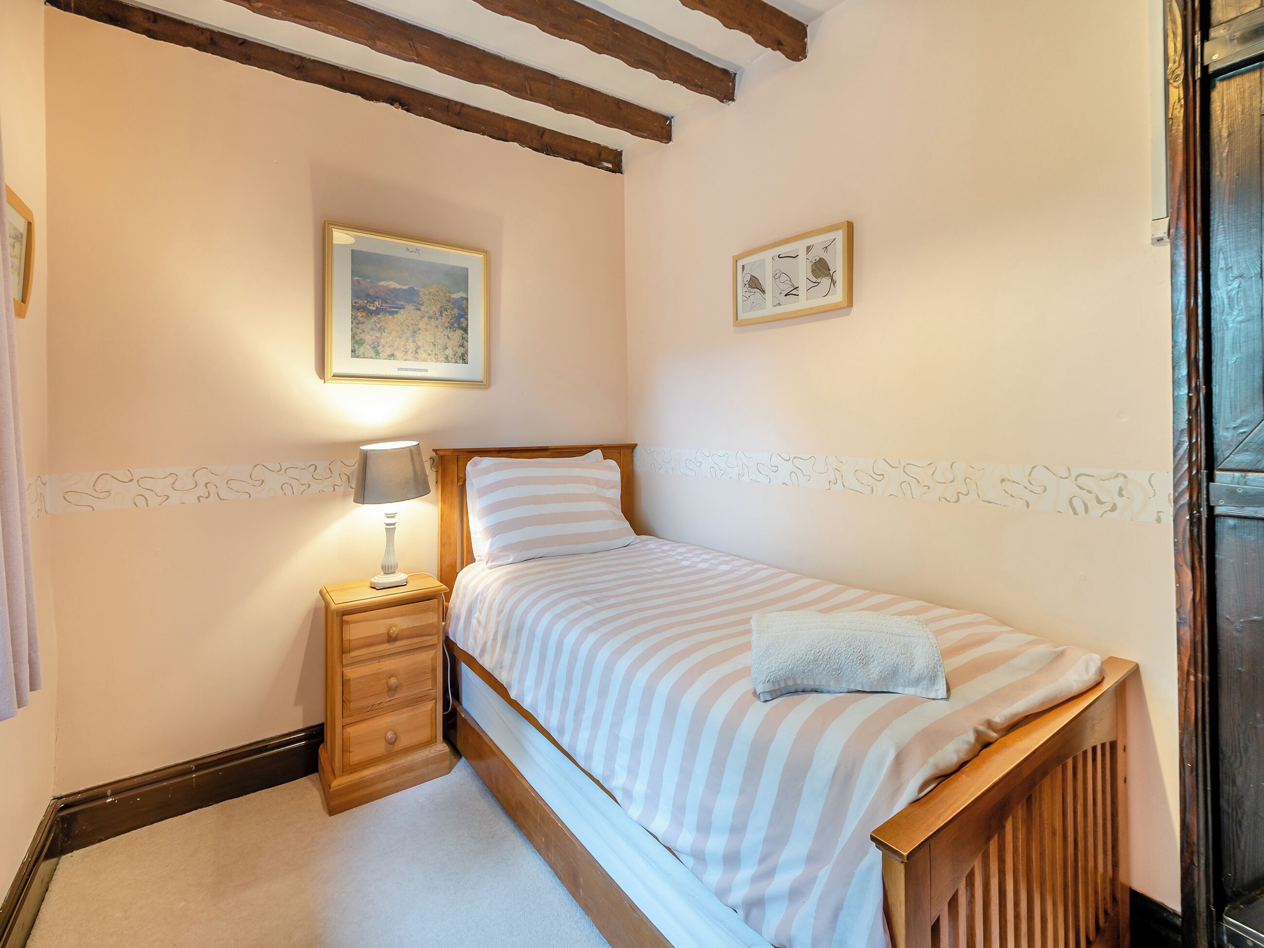 Un lit simple avec une couvre-lit à rayures, une table de chevet avec une lampe et deux tableaux encadrés accrochés au mur.
