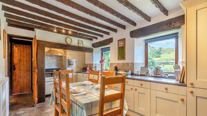 Una cocina con vigas de madera, una mesa de comedor con sillas, armarios blancos y vistas al exterior a través de una ventana.