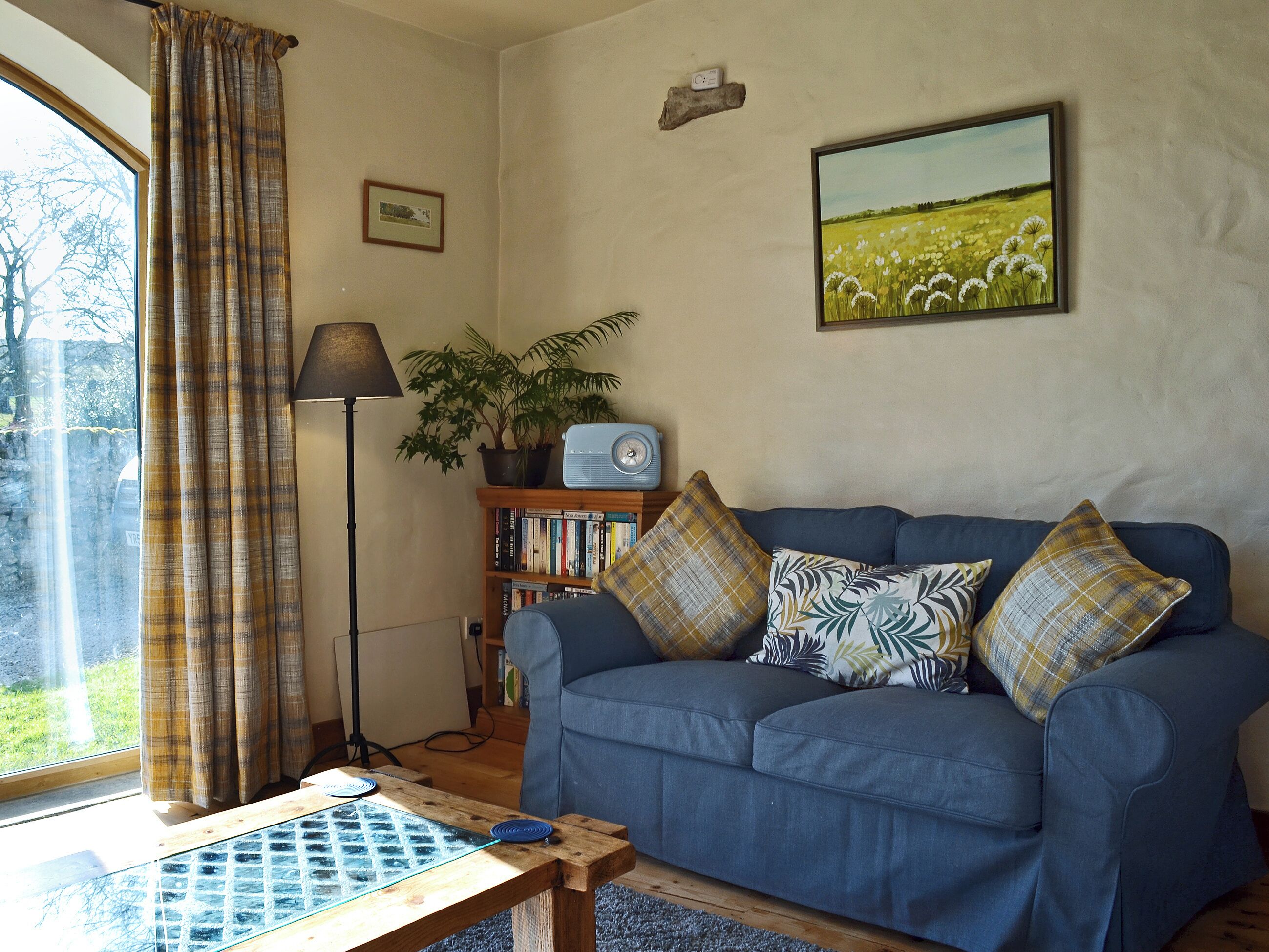 A living room with a blue sofa, a coffee table, a bookshelf, a lamp, and a painting on the wall.
