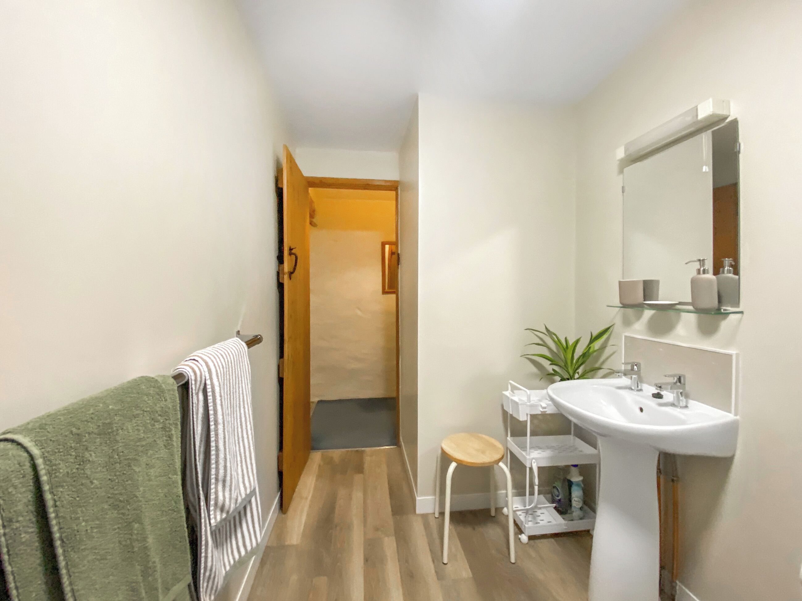 A bathroom with a wooden floor, a white sink, a mirror, and a green towel on a rack.