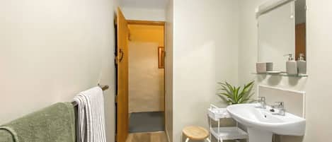 A bathroom with a wooden floor, a white sink, a mirror, and a green towel on a rack.