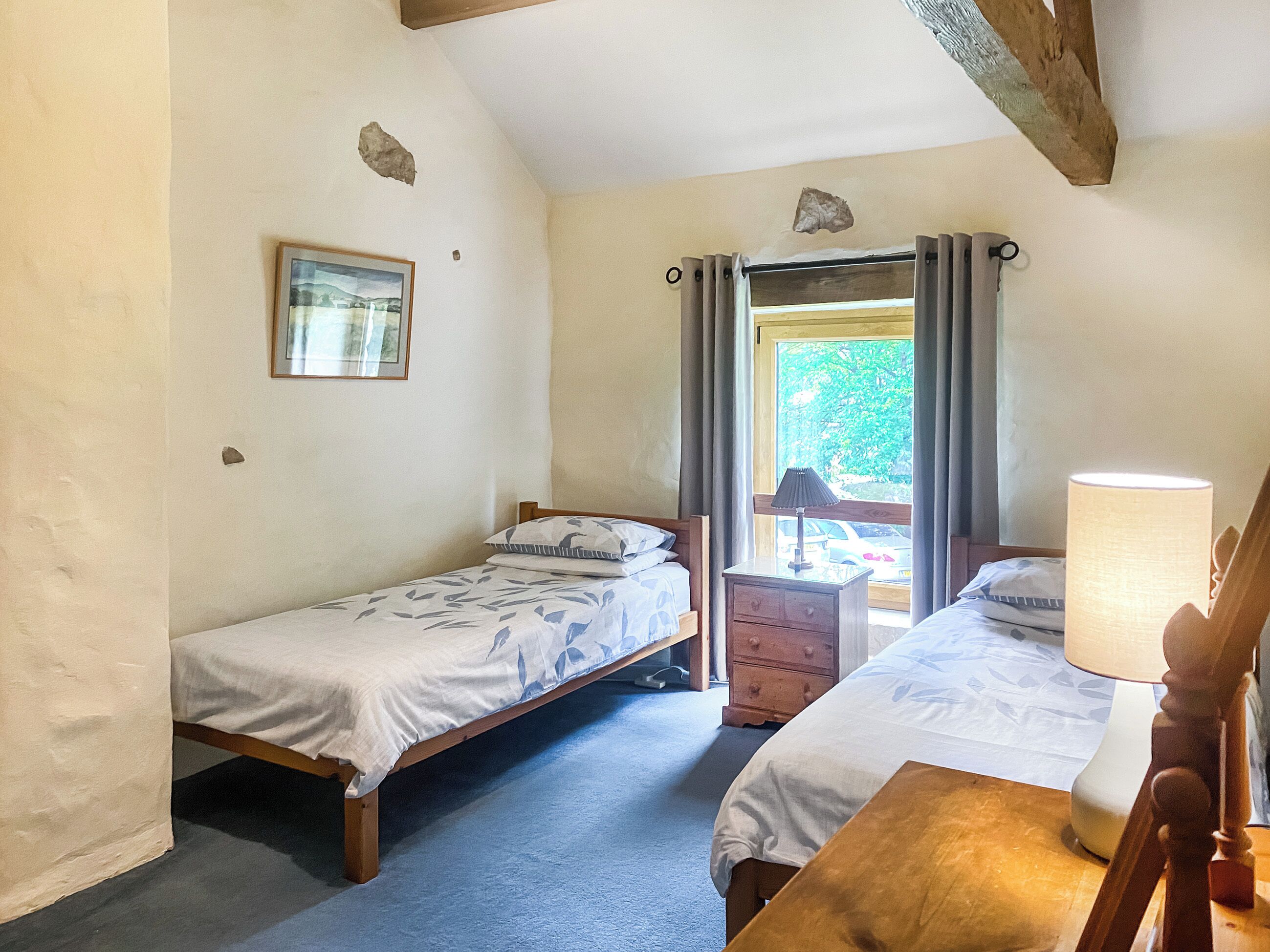 A small, cozy bedroom with two single beds, a wooden nightstand, a table, and a window with curtains.