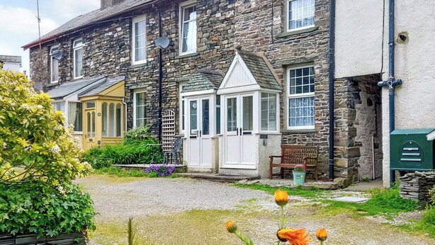 A stone house with a traditional design, featuring a front porch, a small garden with flowers, and a bench.