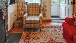 A cozy living room with a plaid armchair, a red sofa, a patterned rug, and a stone fireplace.